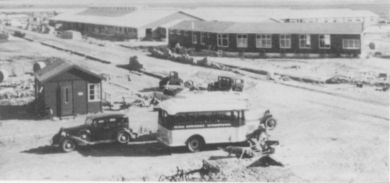 Group of single-level buildings with a shack, cars, and a bus in foreground