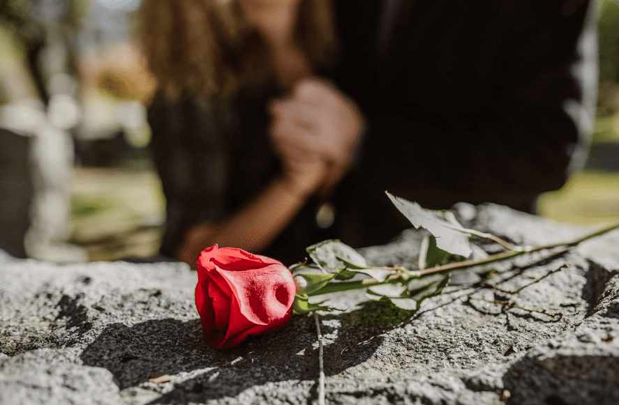 Photo of rose on a grave stone with two figures in the background, representing grief