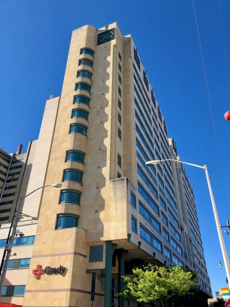 Photo of the modern Grady Memorial Hospital, a tan building with around 15 floors and many windows with its name on the side of the building.
